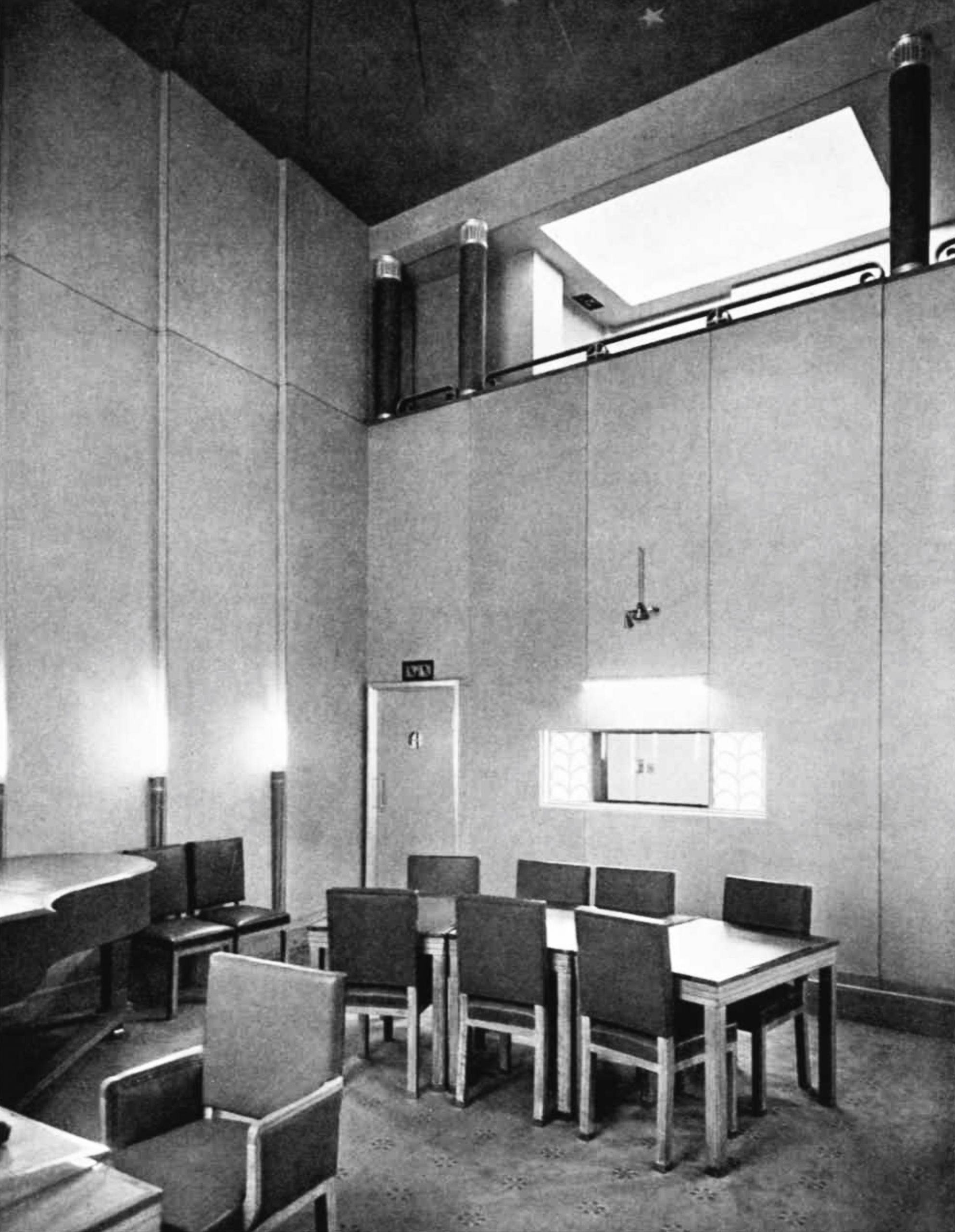 A tall room with a piano, desk and many chairs