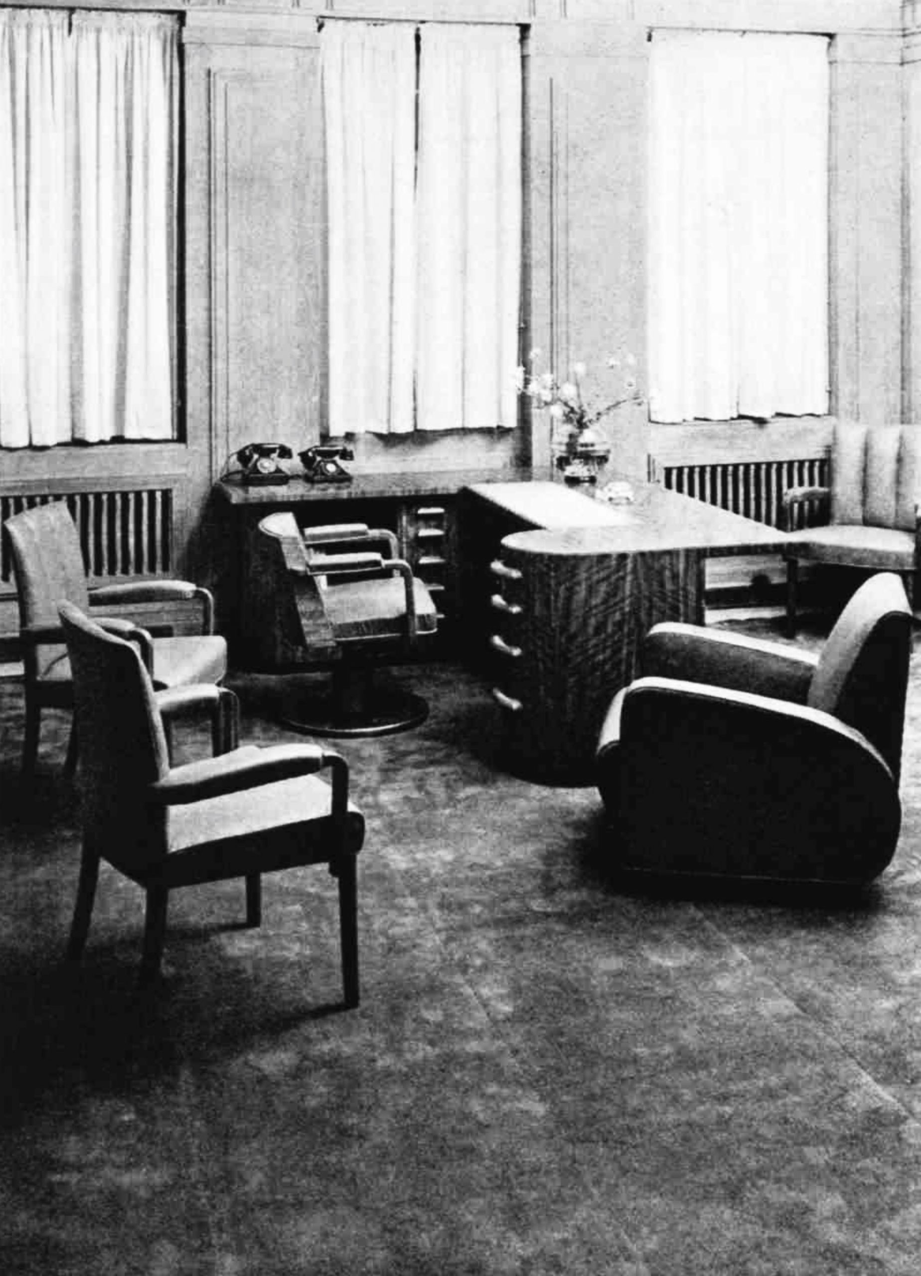 A office with a fitted desk with two telephones surrounded by 5 chairs in 3 different styles