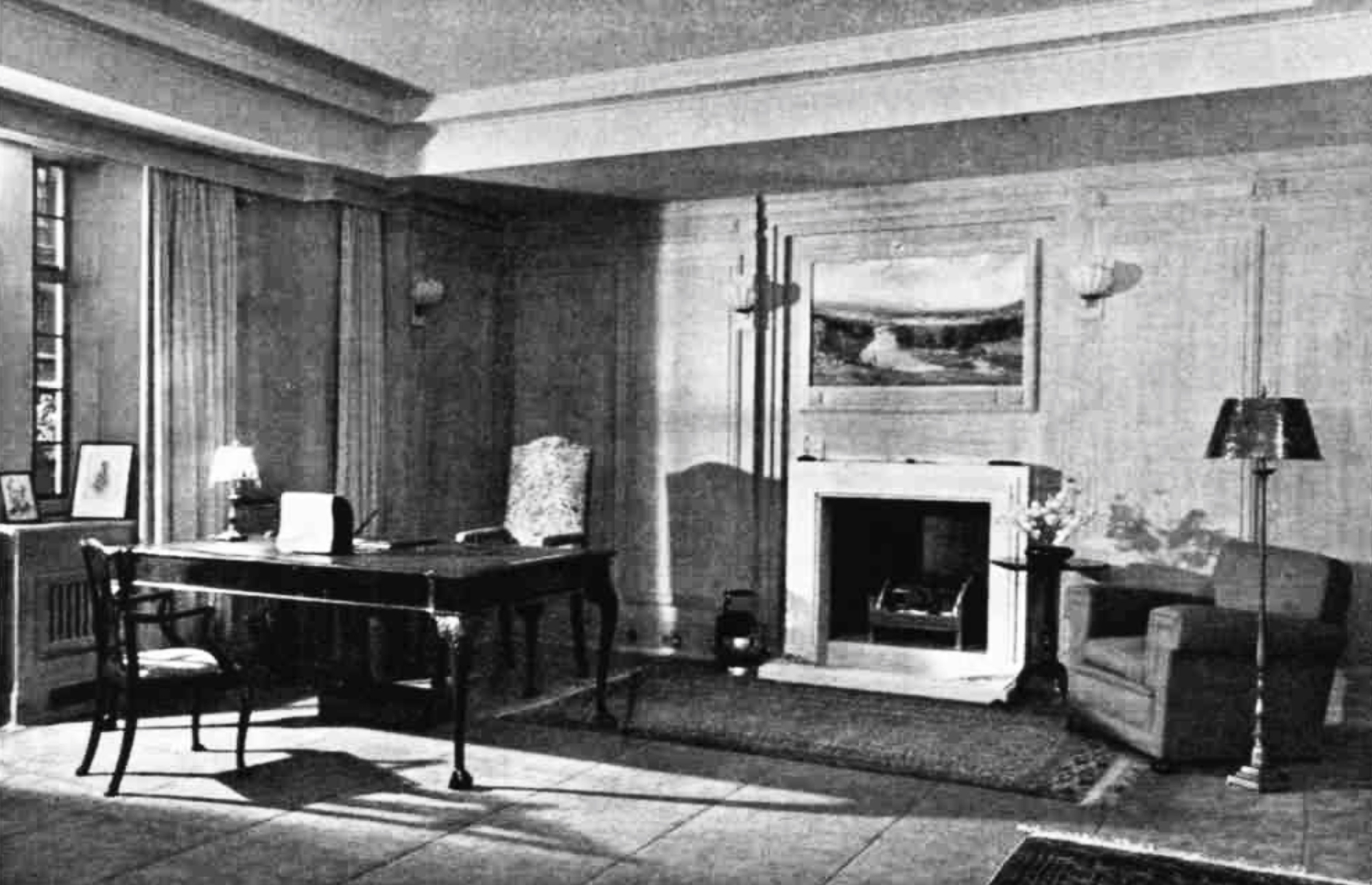 A room with wooden walls, a fireplace and an ornate desk with one commanding chair and one basic chair